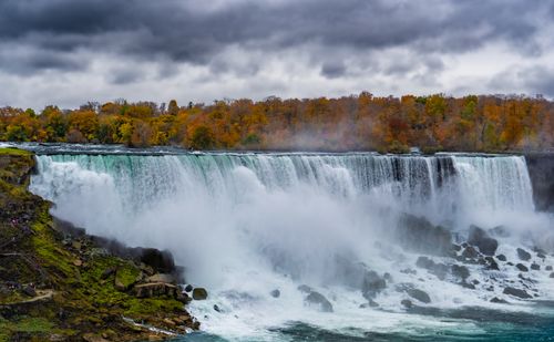 Free Stunning view of Niagara Falls surrounded by vibrant autumn foliage under dramatic skies. Stock Photo