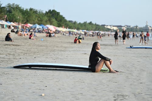 Surfer Sits by Surfboard on Beach