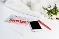 优雅的构图中，生日贺卡、智能手机、蜡烛与白玫瑰相映成趣，营造出时尚的问候氛围