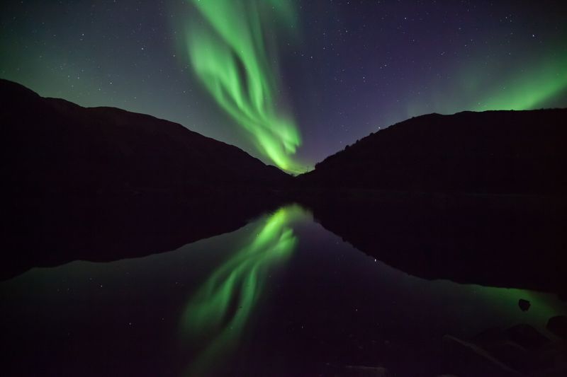 Aurora boreală verde reflectată în lacul liniștit sub cerul înstelat