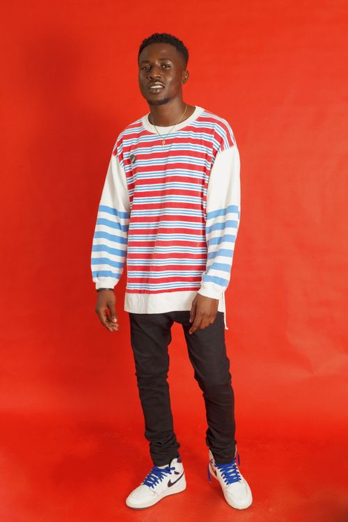 Free Portrait of a stylish young man wearing a colorful striped sweater and black pants, standing confidently. Stock Photo