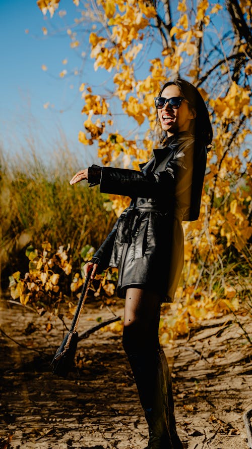 Laughing Model in a Leather Coat Under a Tree with Golden Autumn Leaves