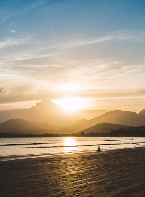 Person Sitting on Beach during Golden Hour
