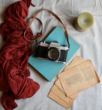 Vintage camera with notebooks, red scarf, and candle on a striped surface. Perfect for creative projects.