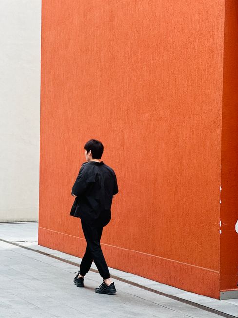 Young adult walks by a vibrant orange wall, creating a striking contrast in urban Shenzhen.