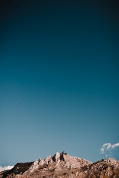 A breathtaking view of a rocky mountain peak with a vast clear blue sky above, perfect for nature-inspired designs.