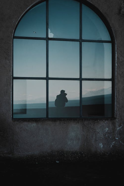 Silhouette Photo of Man Standing Beside Window