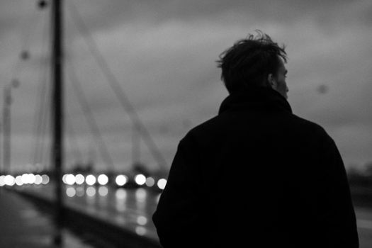 Black and white photo of a man walking on a bridge at night, capturing a serene and moody atmosphere.
