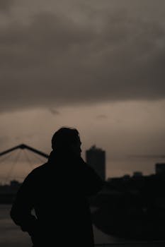 Silhouette of a man against a cloudy urban skyline, evoking a moody atmosphere.