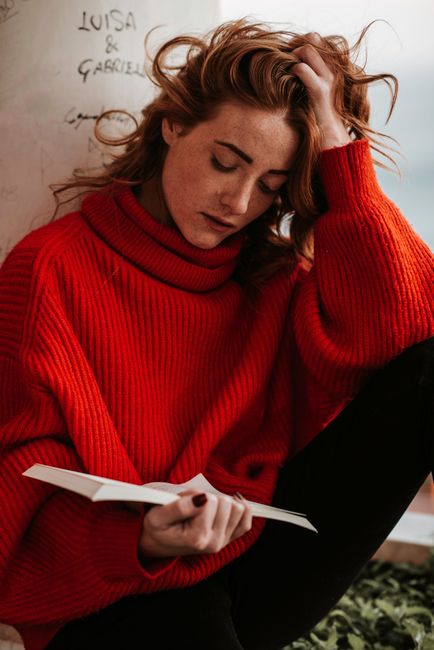 Woman in a red sweater reading indoors, capturing a relaxed and contemplative mood.
