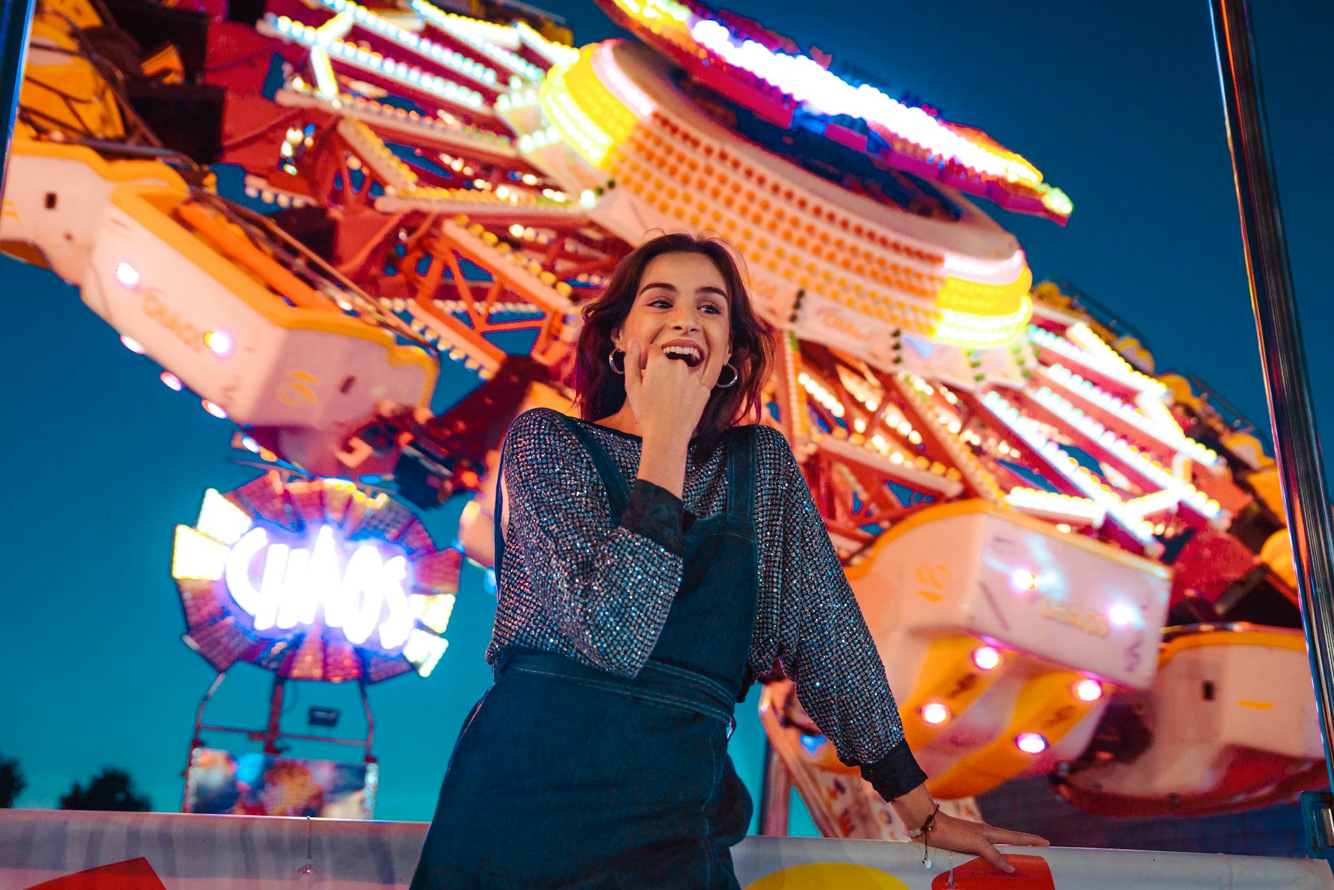 A woman smiles brightly in front of a colorful carnival ride, capturing the night's excitement.