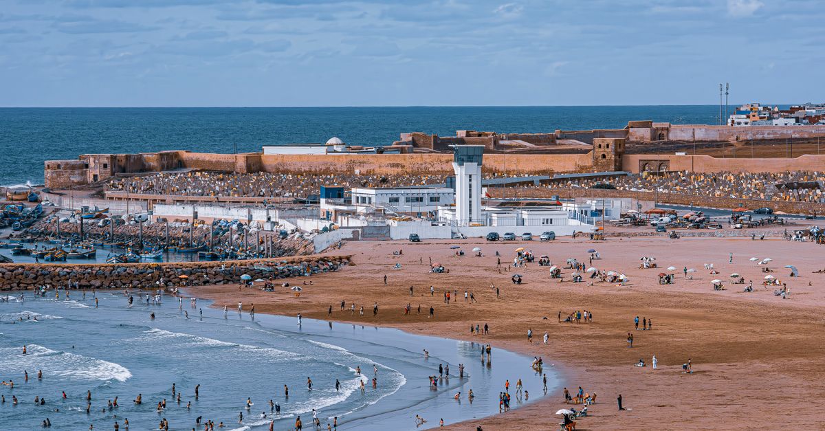 A vibrant beach scene near Rabat's historic fort with people enjoying sun and sea.
