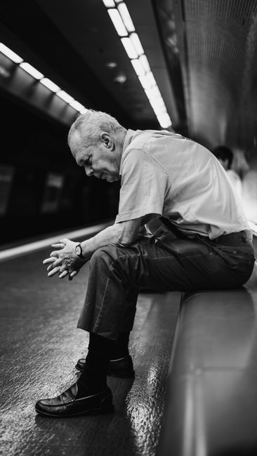 A senior man sits quietly in a subway station, lost in thought and waiting for the next train.