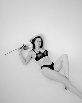Stylish woman in black lingerie holding a flower, in a classic black and white pose.