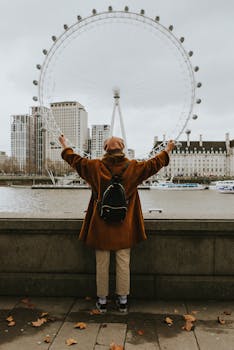 Person with arms raised viewing the London Eye across River Thames in autumn. by Alessio Cesario