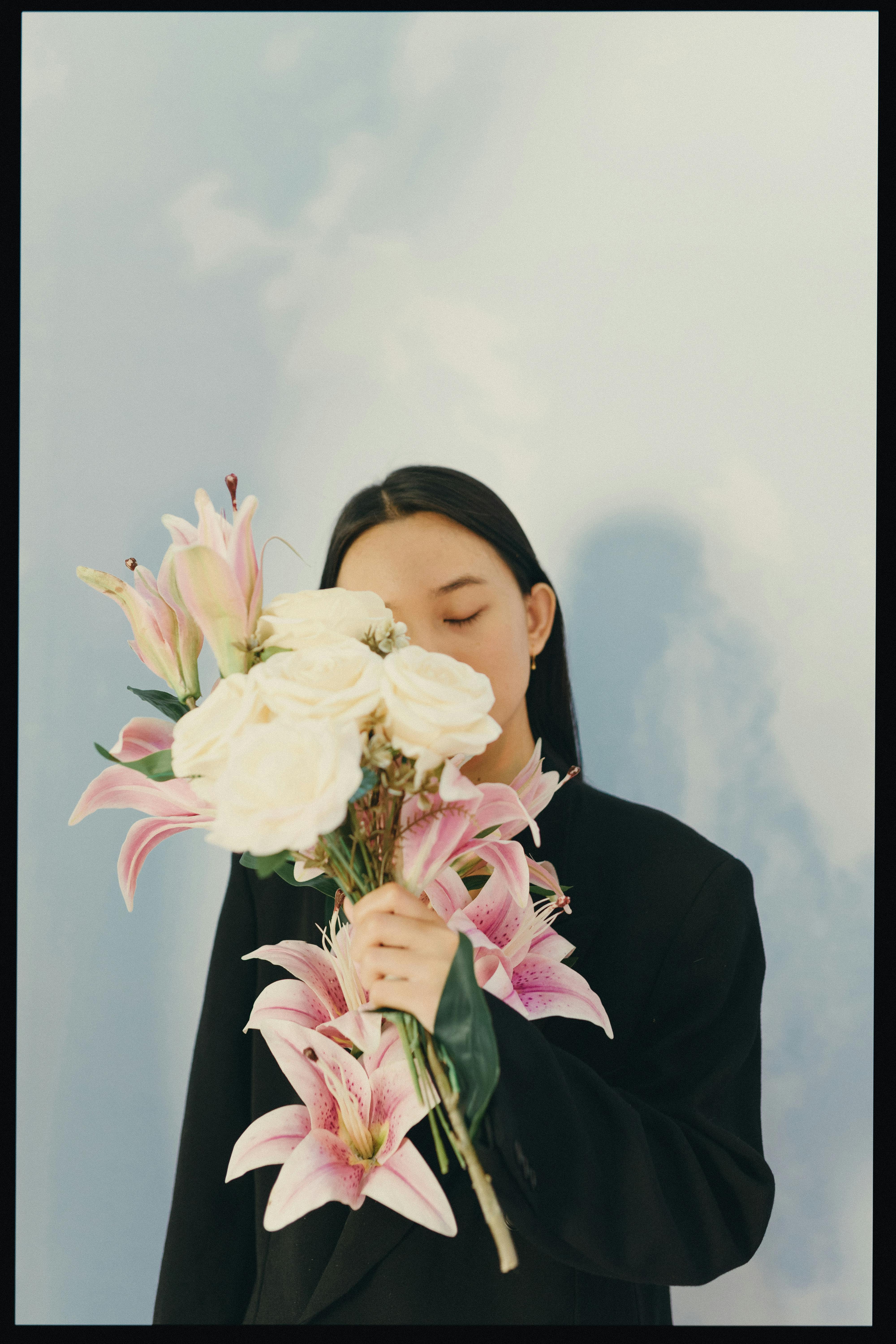 A serene moment with a woman holding a bouquet of lilies and roses against a soft background.
