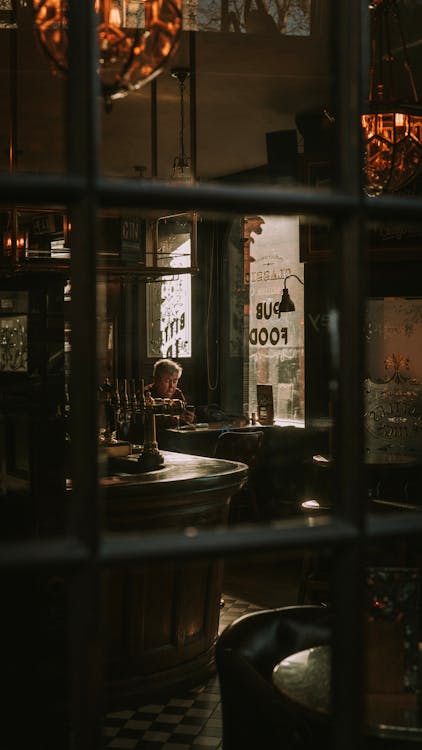 A Lone Person Seated On A Table Of A Cozy Old Pub 
