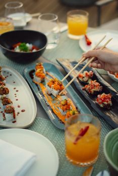 Hand using chopsticks to pick up sushi from a beautifully arranged platter at an outdoor setting.