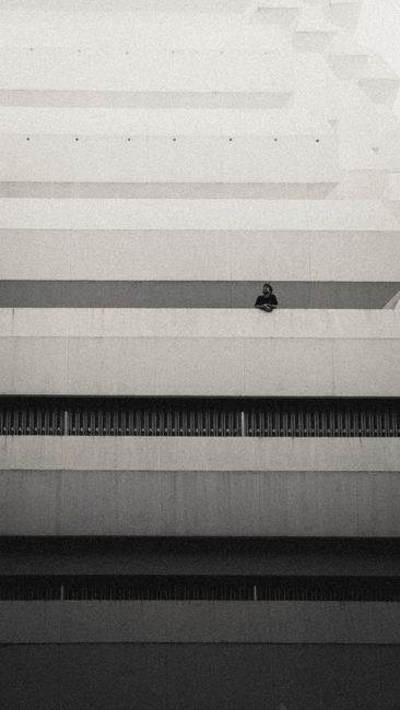 Monochrome photo of a person on a modern building's balcony, showcasing minimalist architecture.