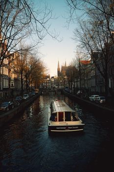 Charming Amsterdam canal with boat cruise during sunset, showcasing historic architecture and serene ambiance.
