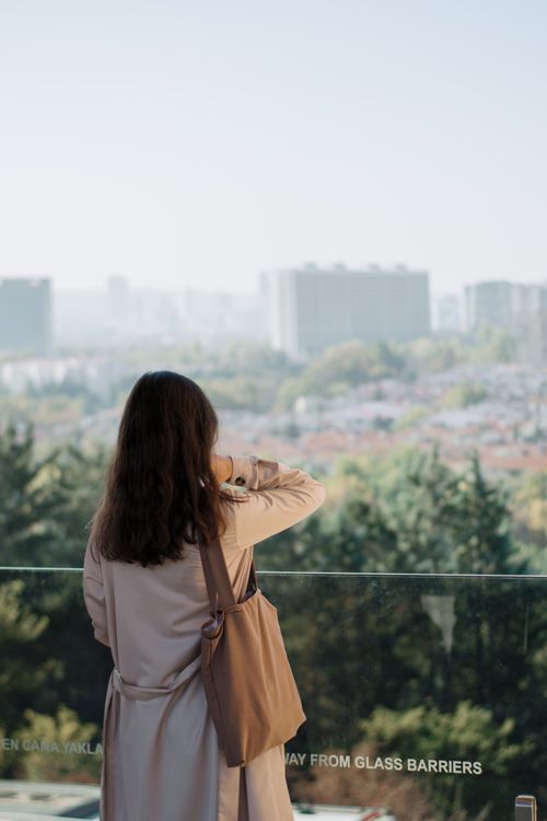 Free A woman standing on a balcony, gazing at a lush green cityscape with buildings in the distance. Stock Photo