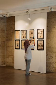 A woman photographs vintage newspapers at a museum exhibition. - Fotografer Sidoarjo