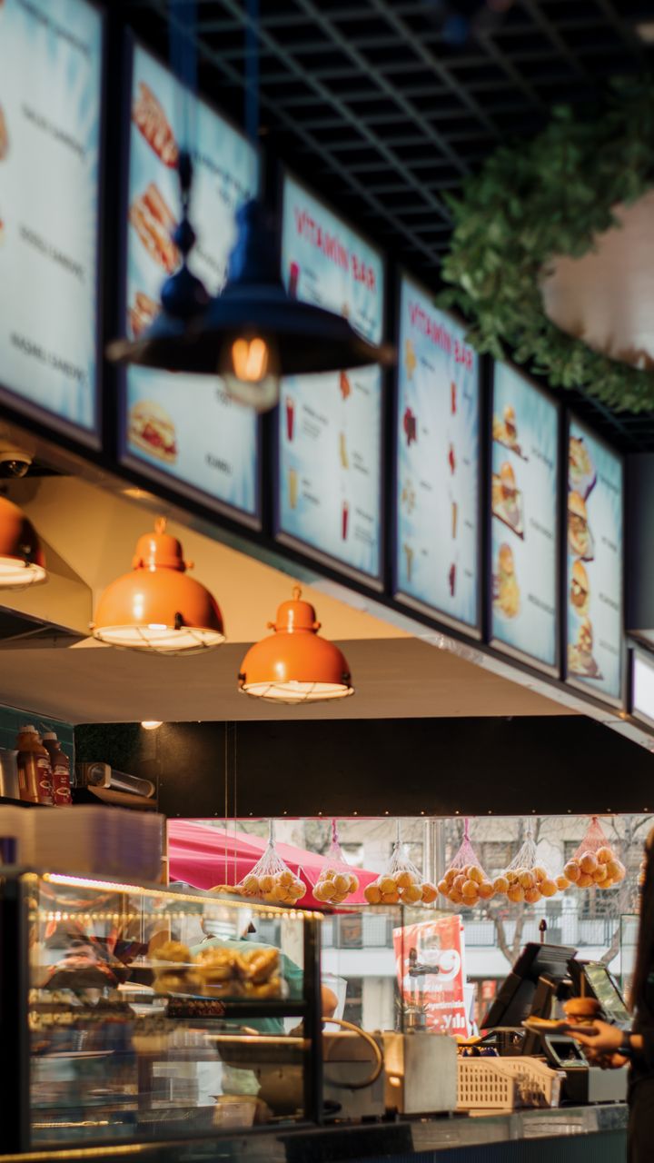 Small digital menu screen displaying drink options mounted next to a modern office coffee bar