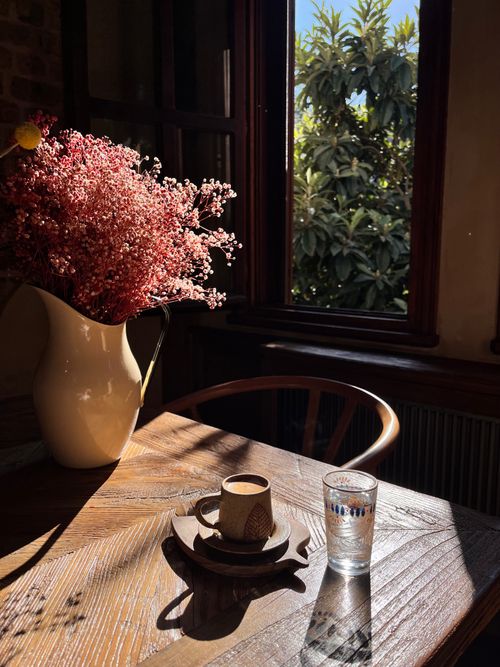 Free Warm sunlight illuminates a cozy dining room with coffee, a vase of flowers, and a window view. Stock Photo