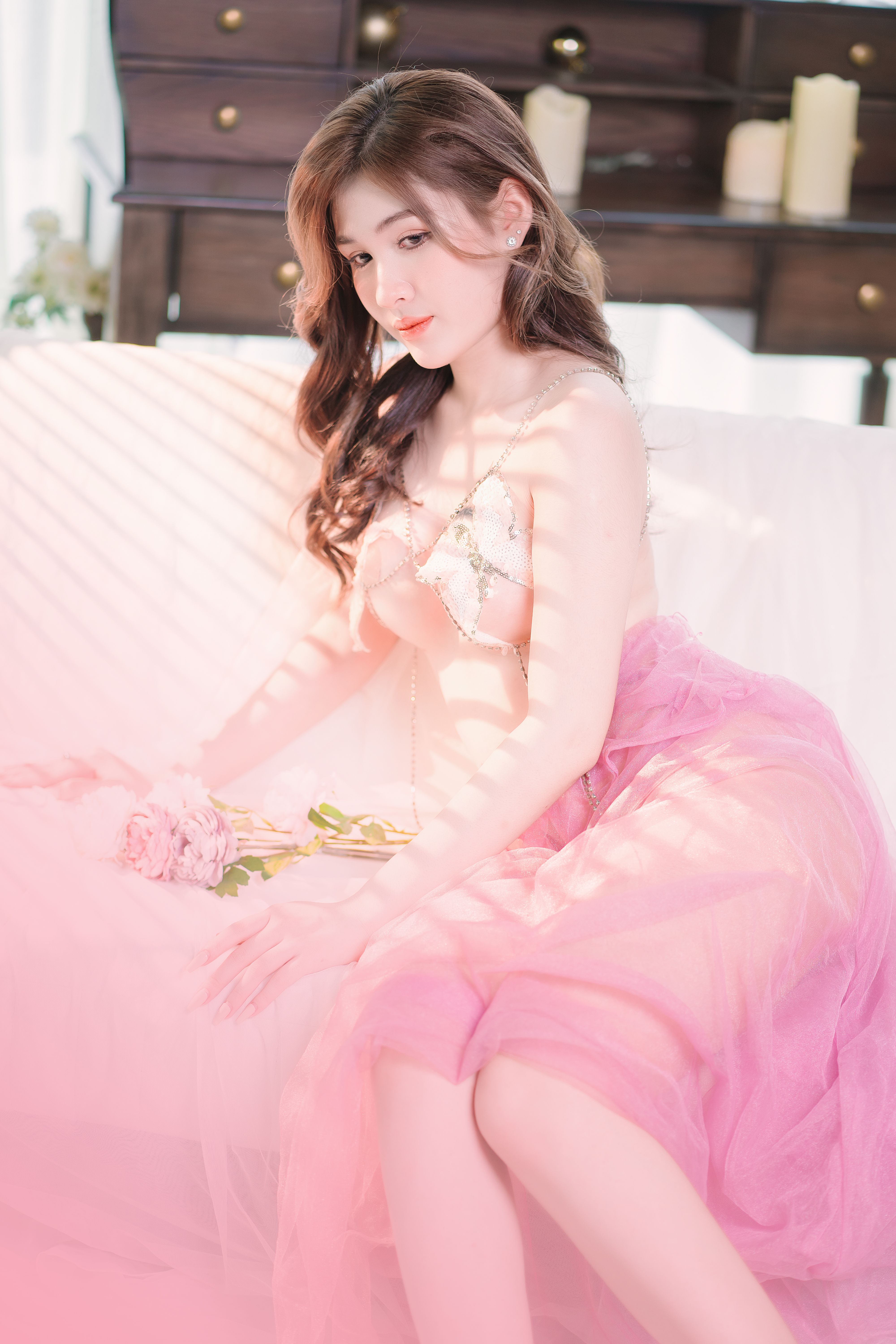 A woman in a pink tulle skirt sits elegantly indoors, bathed in soft light.