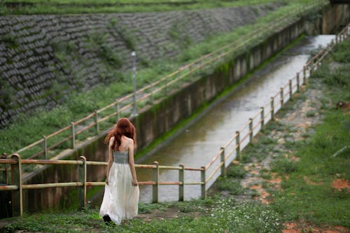Redhead Woman in a Long Dress Walking by a Canal