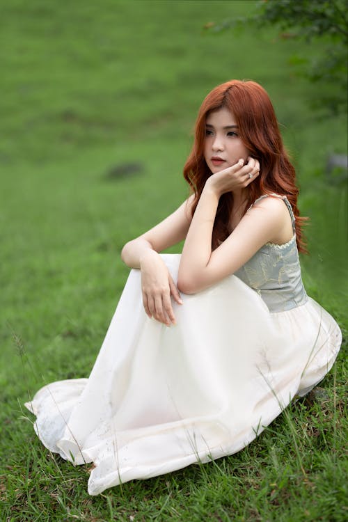Young Woman in a White Dress Sitting on the Grass