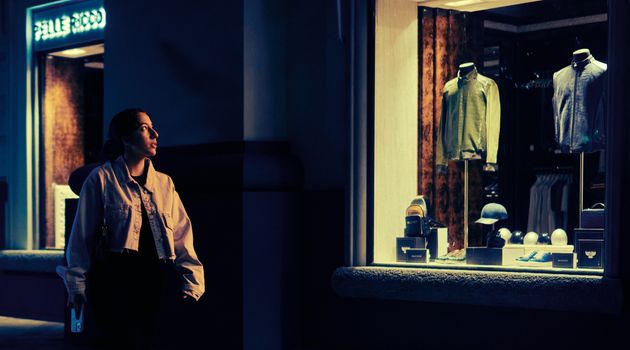 A woman looking at an illuminated shop window display in an urban setting at night.