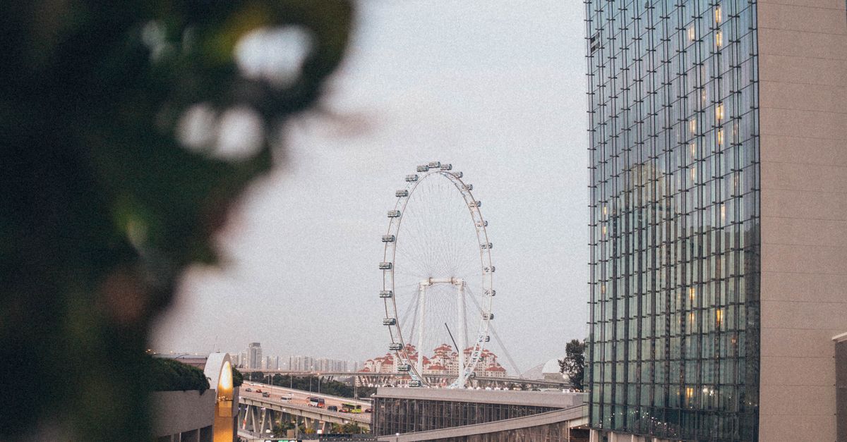 Vibrant city view featuring a ferris wheel, skyscraper, and busy road at dusk.