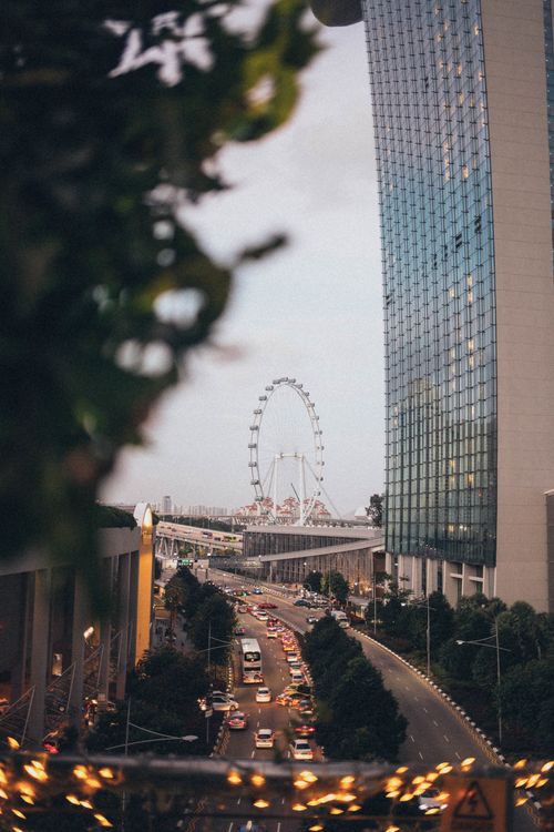 Free Vibrant city view featuring a ferris wheel, skyscraper, and busy road at dusk. Stock Photo