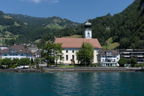 Free Picturesque church overlooking Lake Lucerne in Gersau, surrounded by lush mountains and serene water. Stock Photo
