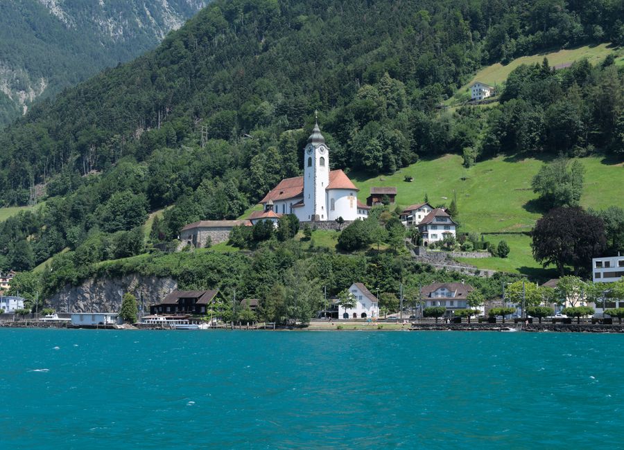 Discover the stunning Pfarrkirche Herz Jesu nestled in Flüelen, Switzerland, framed by lush green hills and Lake Lucerne.