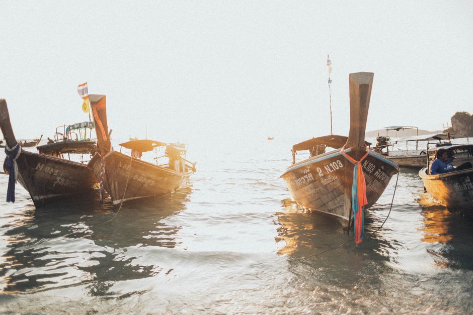 Sunlit scene of traditional long-tail boats floating on calm waters, creating a serene outdoor setting.