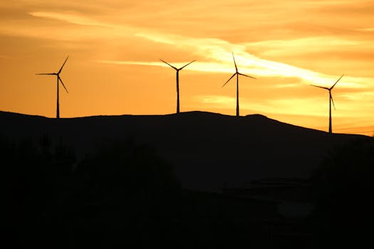 Wind turbines on a hill silhouetted against a stunning yellow sky at sunset.