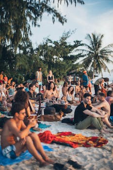 日落时分，一群形形色色的人正围着棕榈树，在海滩上享受热闹的派对