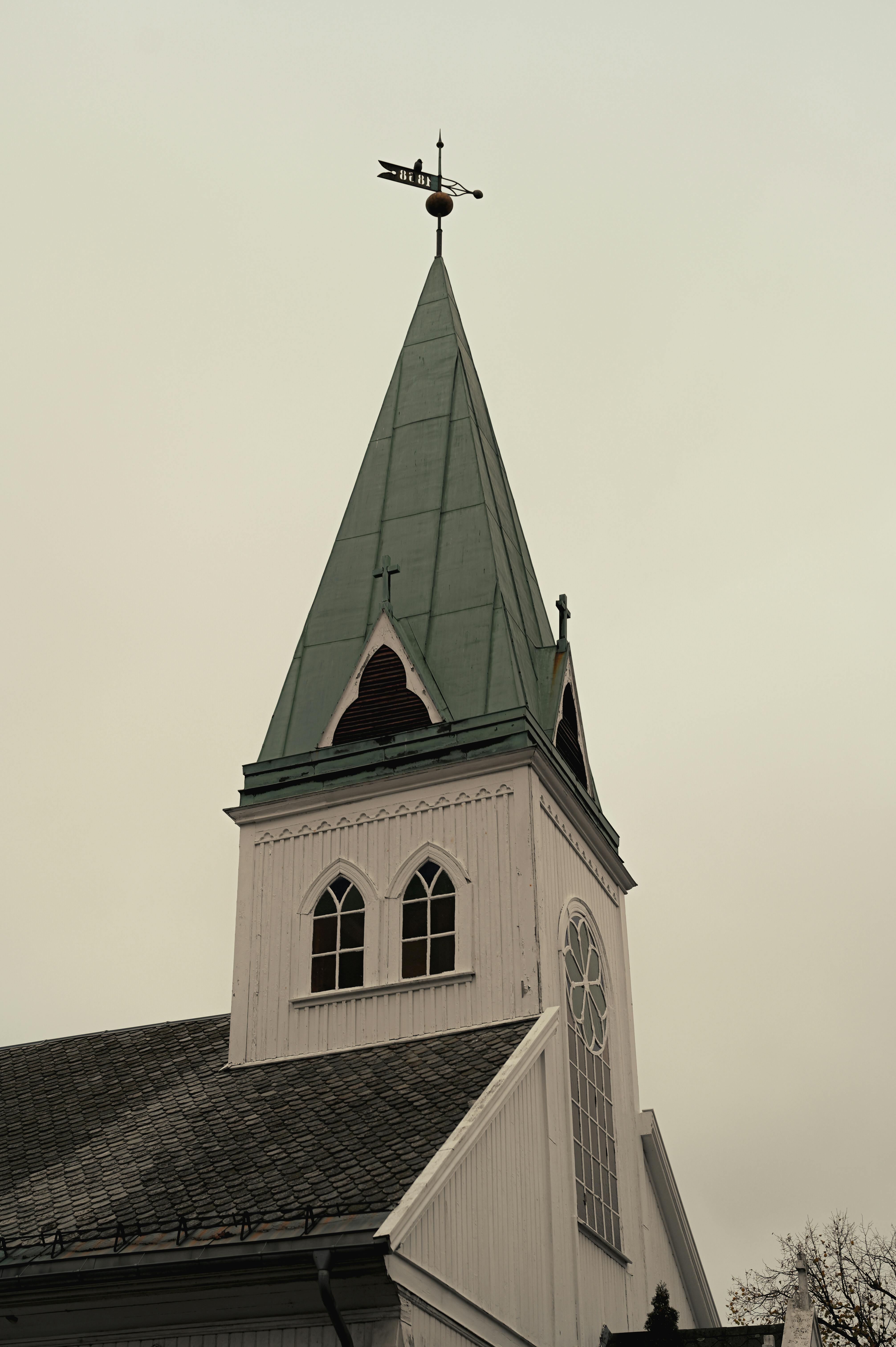 Vertical shot of a Gothic church steeple with a weather vane against a cloudy sky, Kansas, USA.