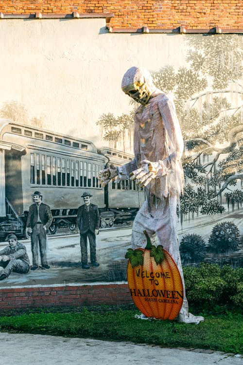 Statue of Skeleton with Pumpkin by Mural on Wall
