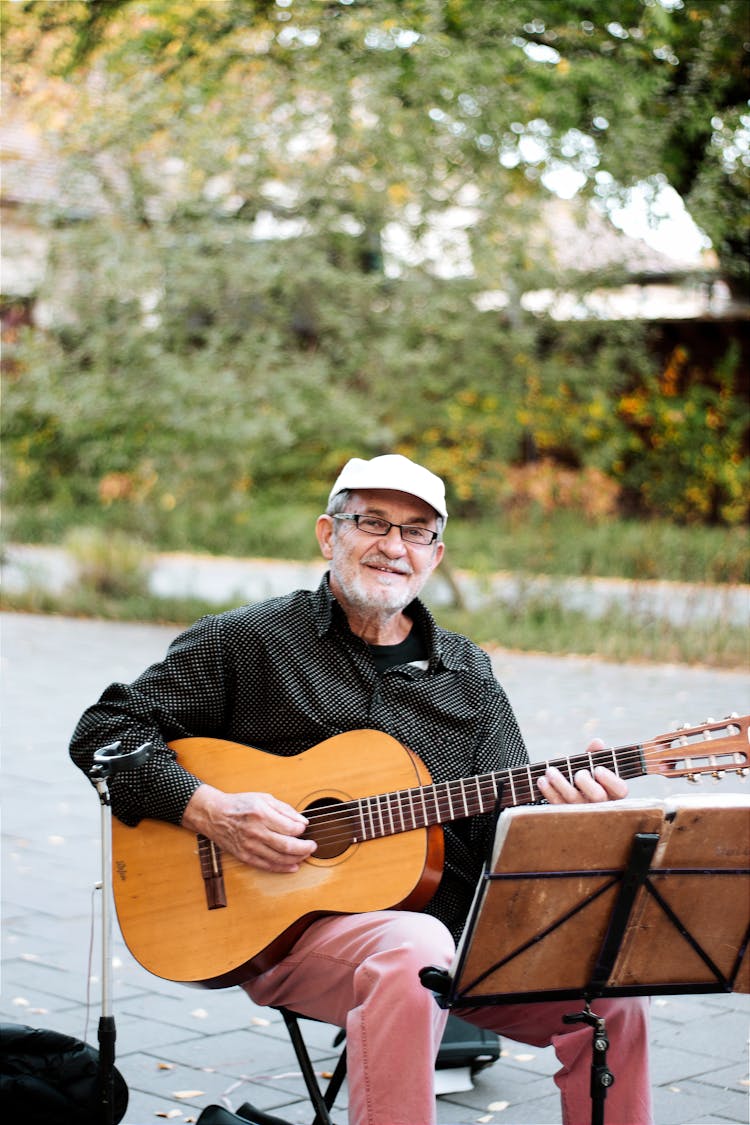 Smiling Man Playing Acoustic Guitar By Stand With Scores