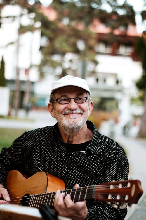 Free Elderly man with glasses and hat plays guitar outside, smiling happily. Stock Photo