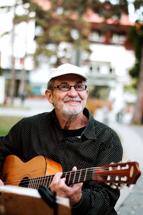 Free Smiling senior playing acoustic guitar in vibrant street scene, Hungary. Stock Photo
