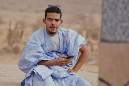 Smiling young man in blue traditional clothing using a smartphone outdoors.