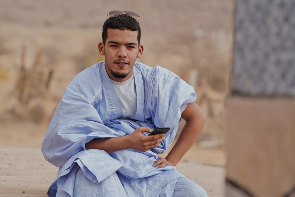 Smiling young man in blue traditional clothing using a smartphone outdoors.