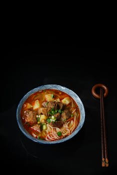 深色背景上特写拍摄的美味牛肉拉面，用筷子夹起