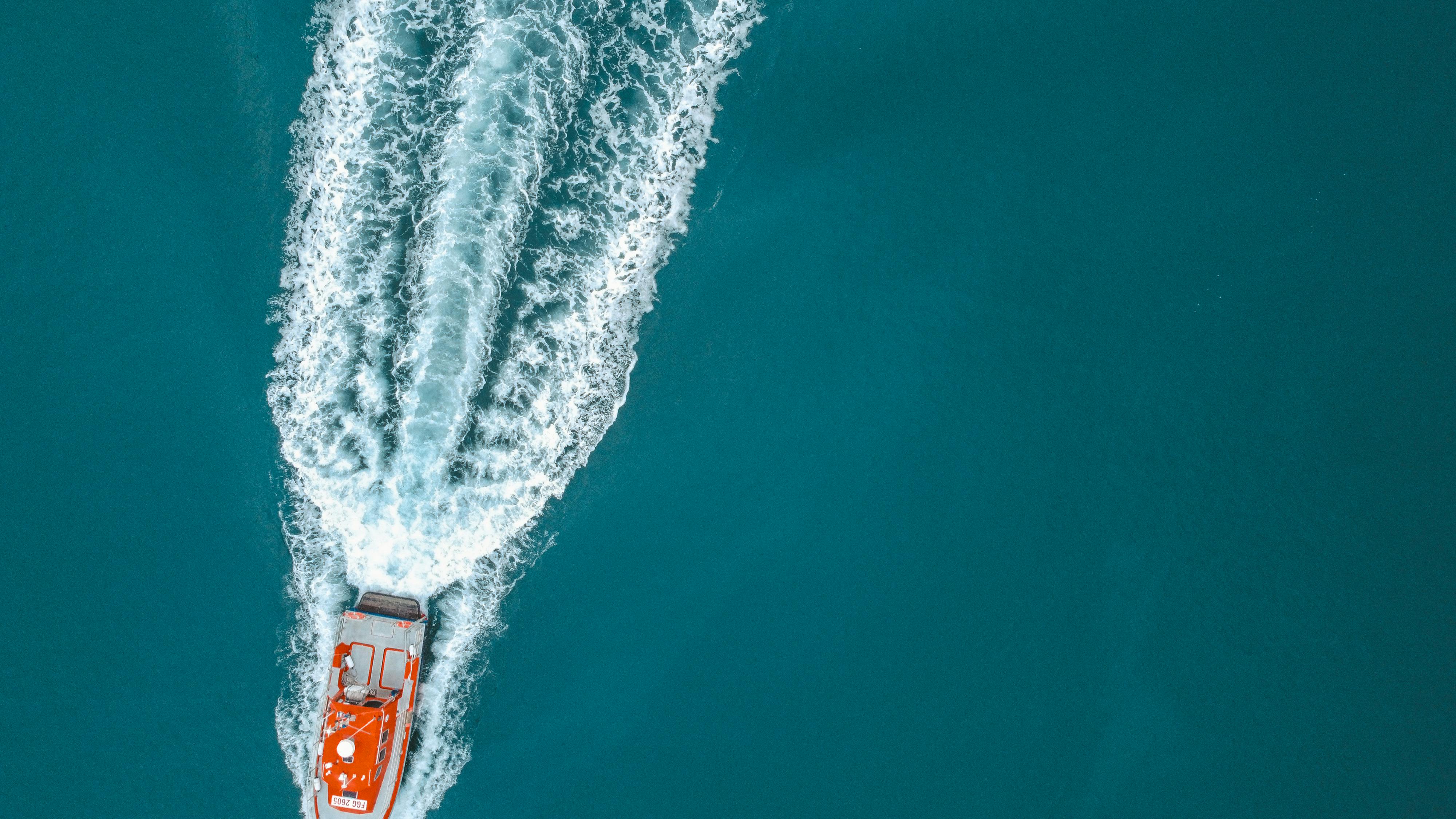 Aerial shot of a red motorboat speeding on the turquoise sea, creating a dynamic water splash.