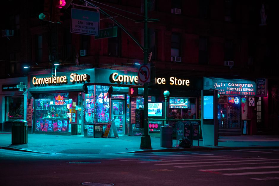 Nighttime view of a neon-lit convenience store in New York City with colorful lighting and empty streets.