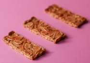 三块美味的杏仁饼干棒陈列在鲜艳的粉色背景上，构成了一幅诱人的小吃展示